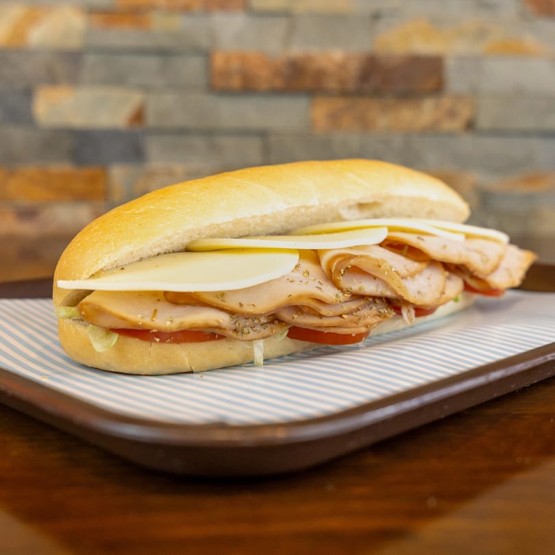 A Megawich turkey and cheese sub sandwich with tomatoes on a striped paper liner.