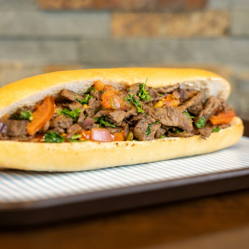 A Megawich sandwich filled with sliced meat, tomatoes, and green herbs on a striped tray.