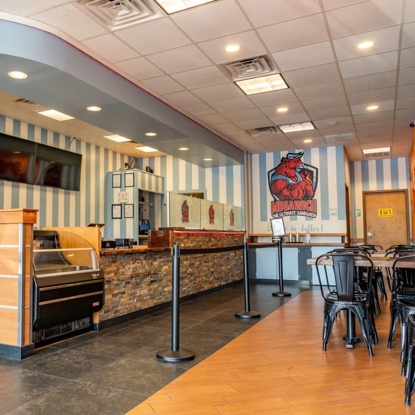Interior of Megawich restaurant with striped walls, a service counter, and dining tables with black chairs.