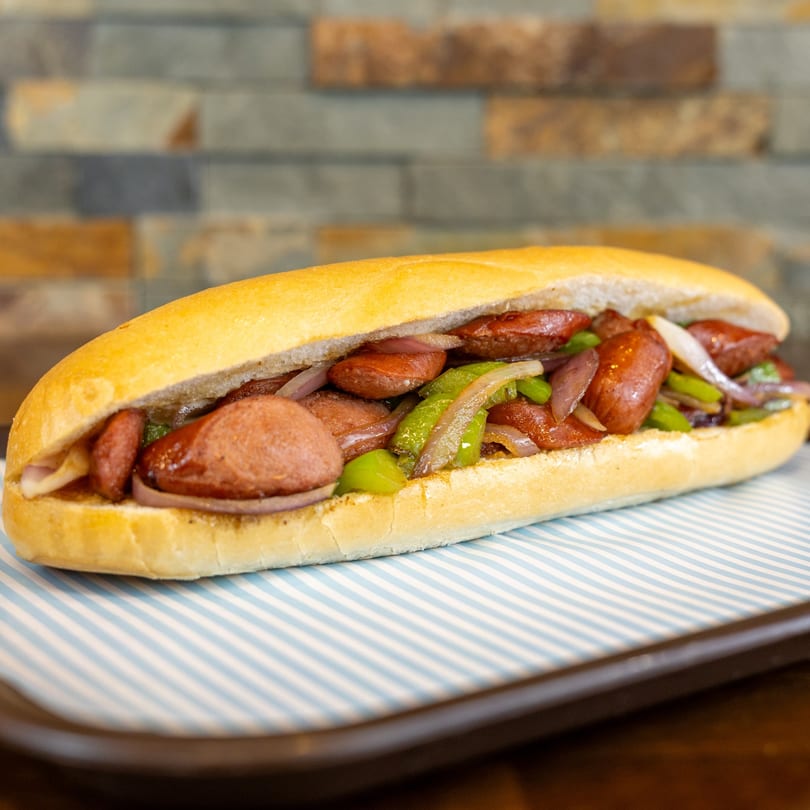 A Megawich sandwich filled with sliced sausage, green peppers, and red onions on a striped paper.