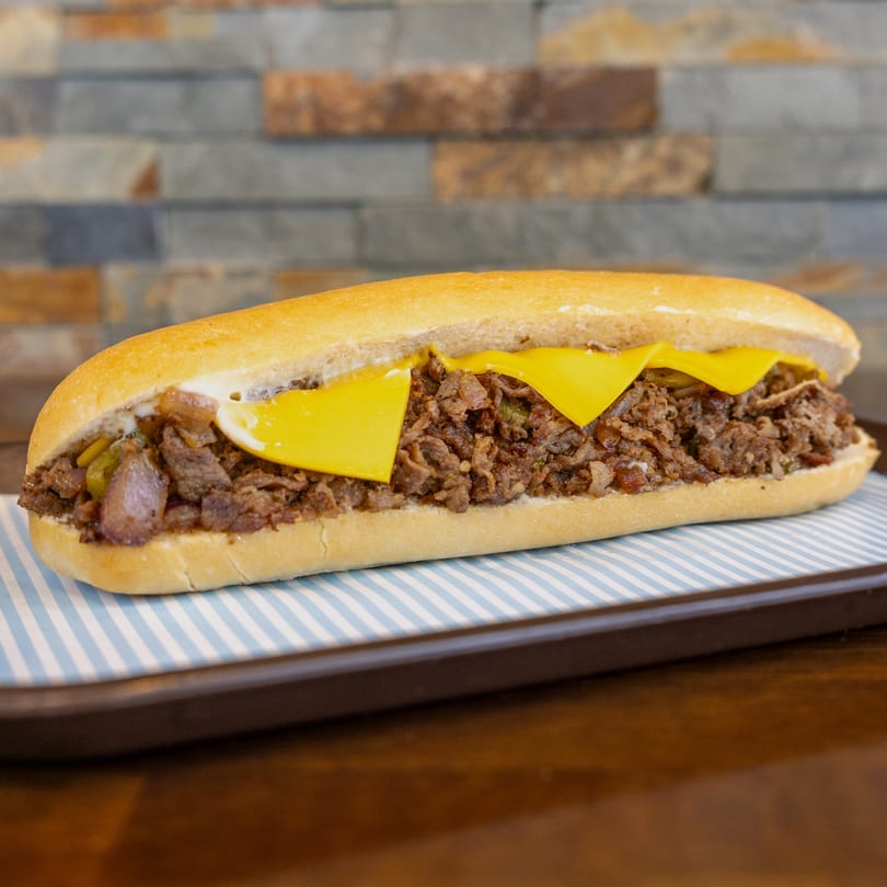 A Megawich cheesesteak sandwich with melted cheese, steak, and onions on a striped paper-lined tray.