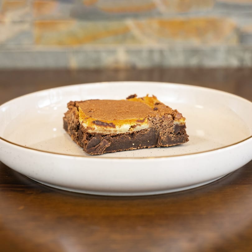 A Megawich brownie with a creamy orange and white topping, dusted with cocoa powder, on a white plate.