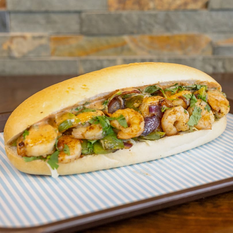 A Megawich shrimp sandwich with green peppers, onions, and cilantro on a striped tray.