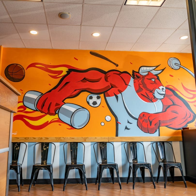 Megawich restaurant interior with a vibrant mural of a muscular bull lifting weights and sports balls.