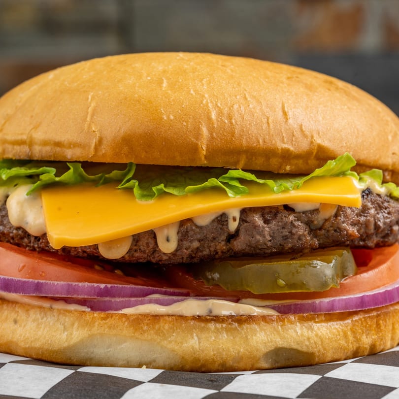 A Megawich burger with cheese, lettuce, tomato, onion, pickles, and special sauce on a bun.